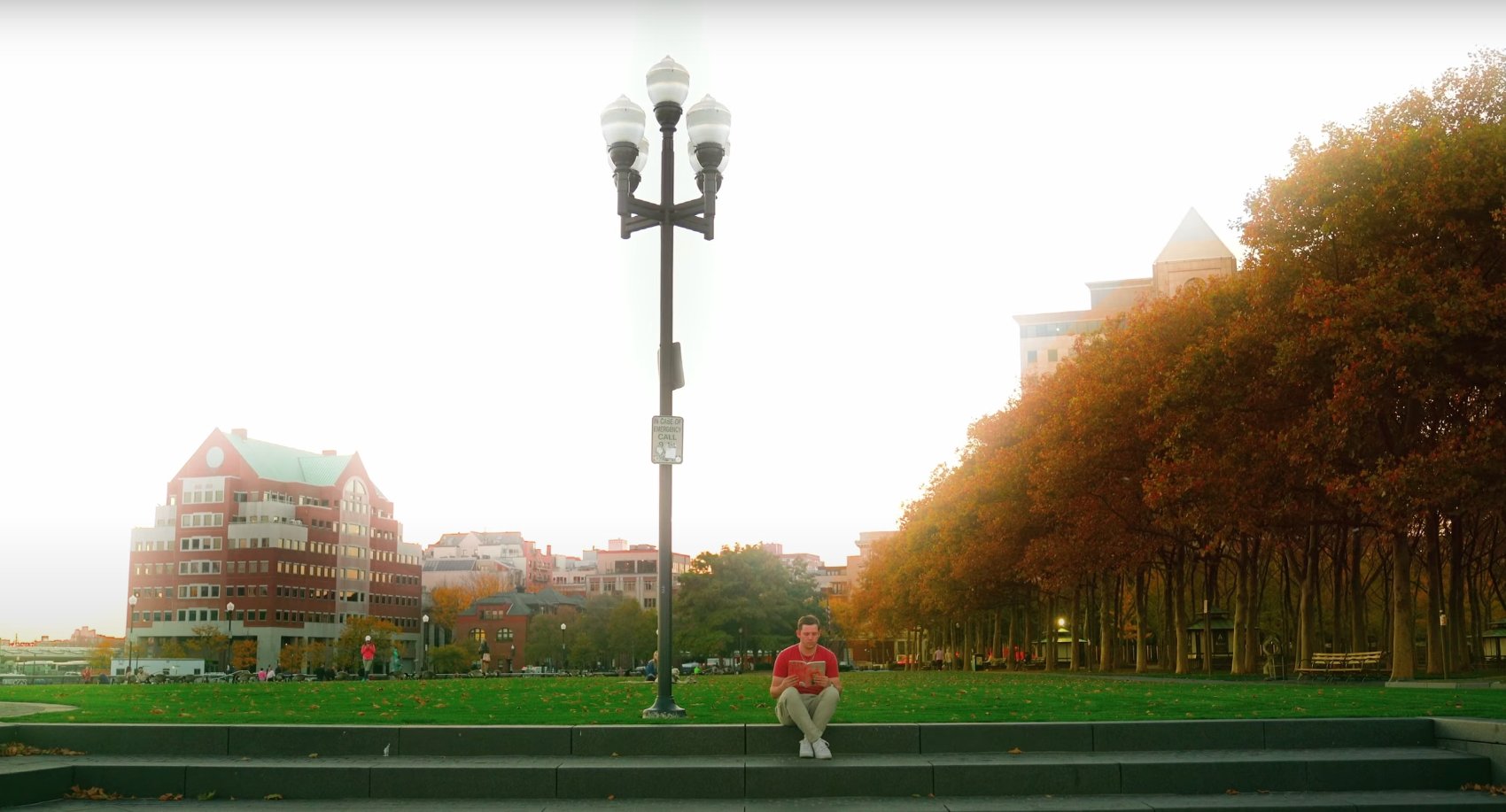 Michael reading on the steps of a park under autumn trees