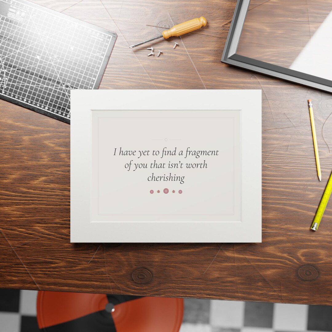 A fine art print in a passepartout paper frame on a workbench, printed with the poem line "I have yet to find a fragment of you that isn't worth cherishing"